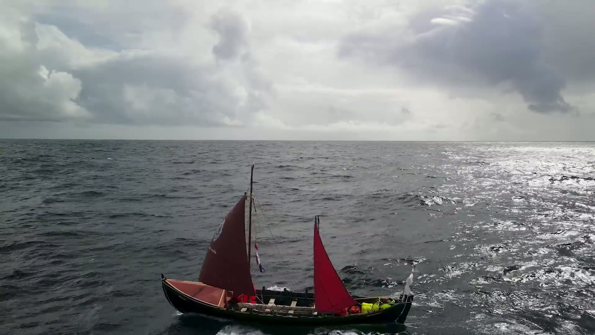 Wikingerboot mit roten Segeln auf offener See unter Sturmwolken, aus der Luft